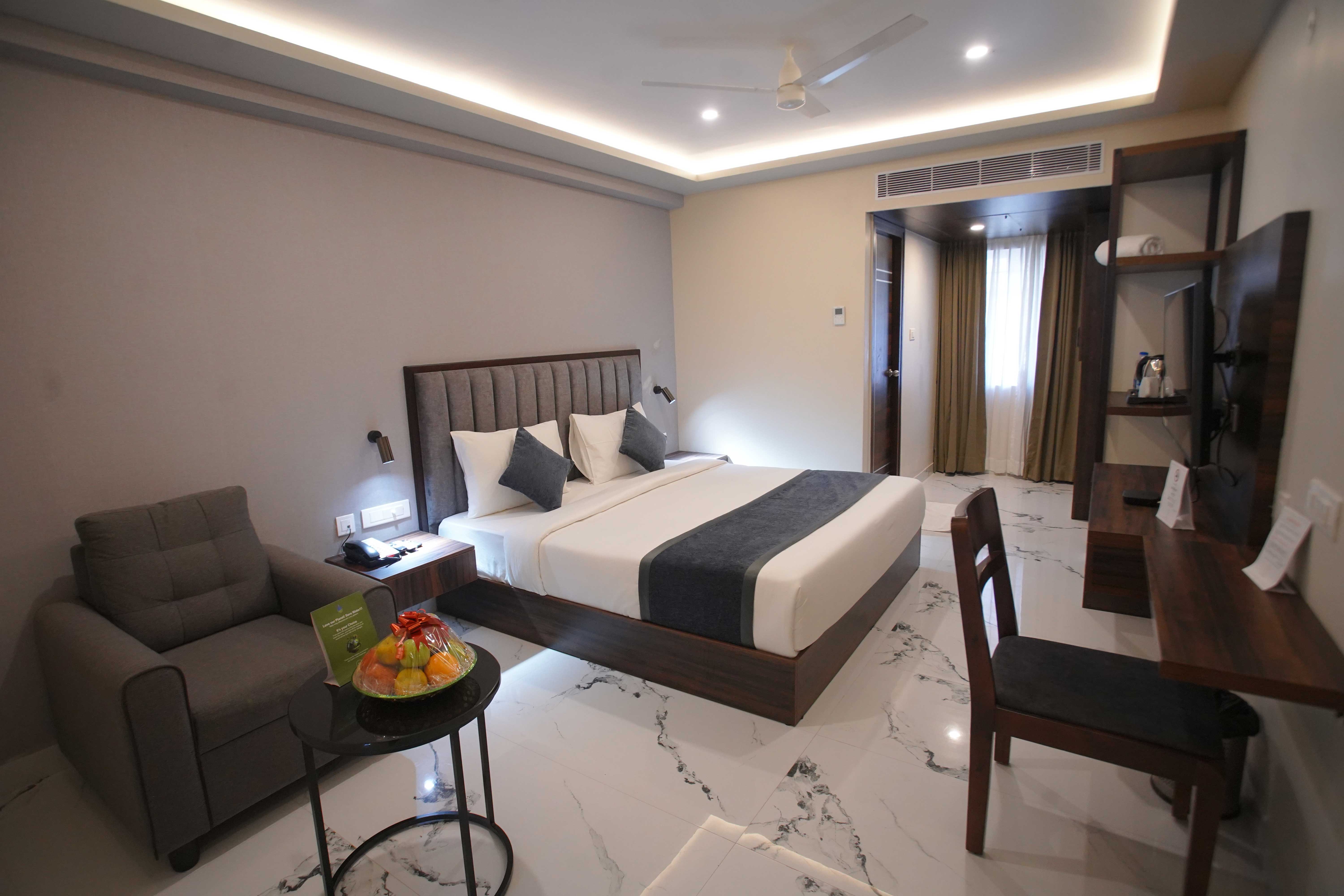 Modern executive room at Bloft Hotel Vellore featuring a plush king-sized bed, lounge chair, and stylish wood furniture in a spacious, well-lit setting.