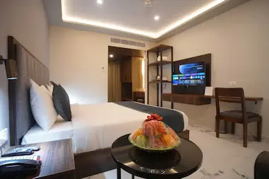 Executive room at Bloft Hotel Vellore showcasing a comfortable bed, smart TV, and complimentary fruit basket on a modern side table.